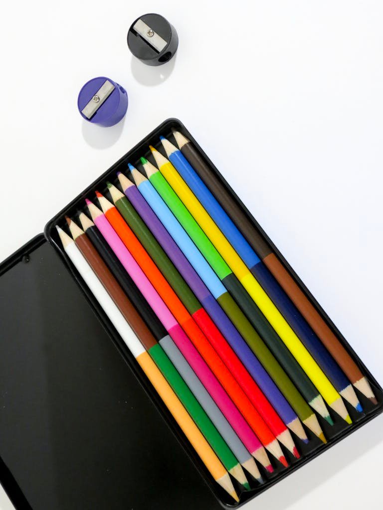 A vibrant display of colored pencils with sharpeners on a white surface, ideal for creative projects.
